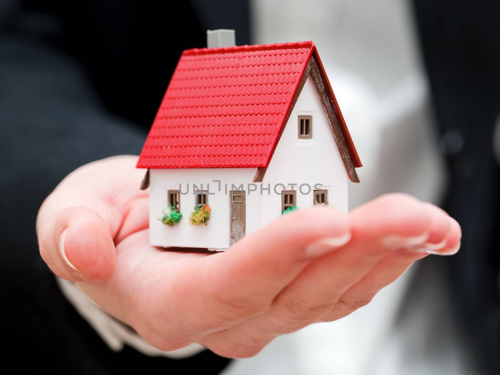 A real estate agent holding a small new house in her hands by photocreo
