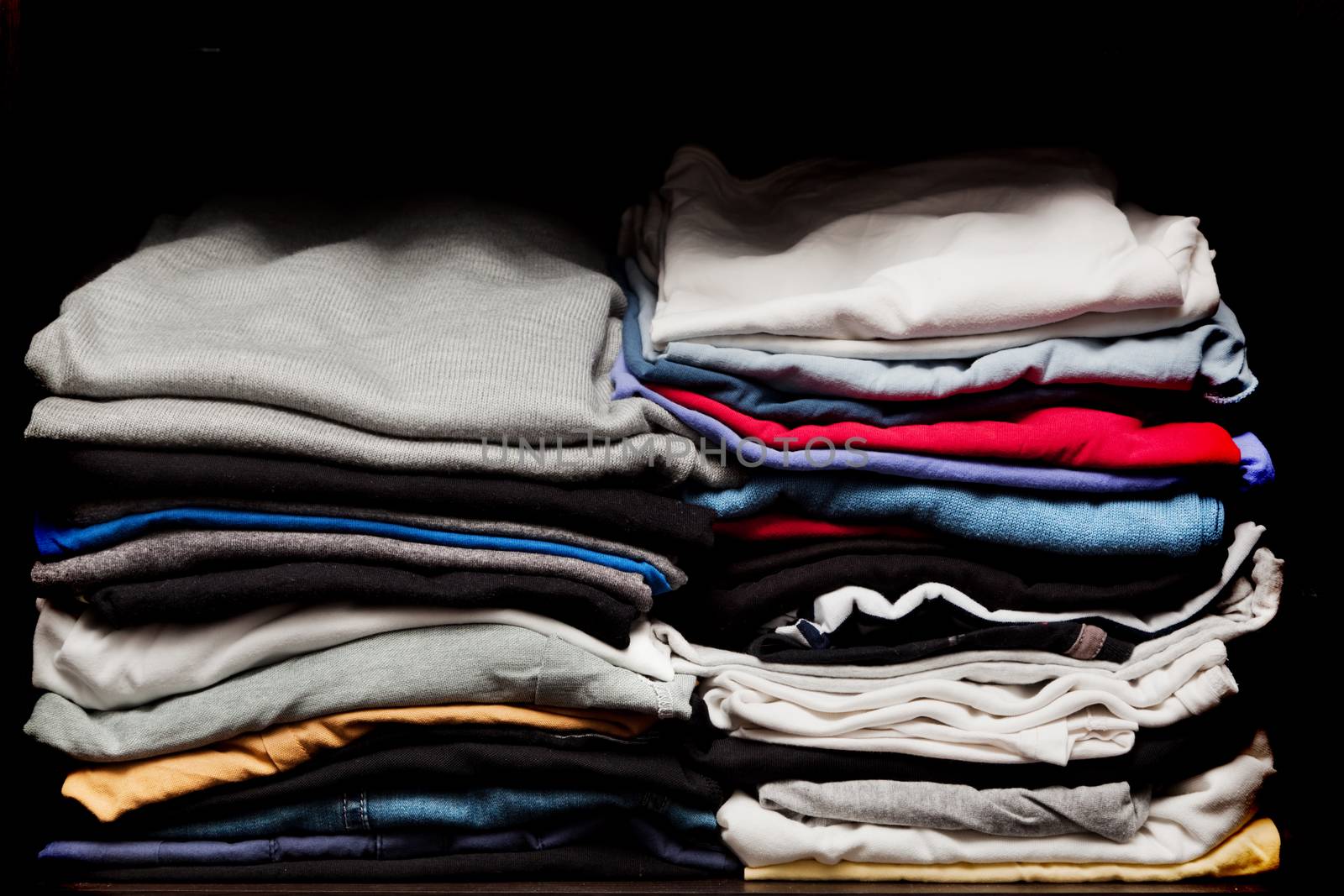 PIles of various clothes from laundry in a wardrobe. Black background
