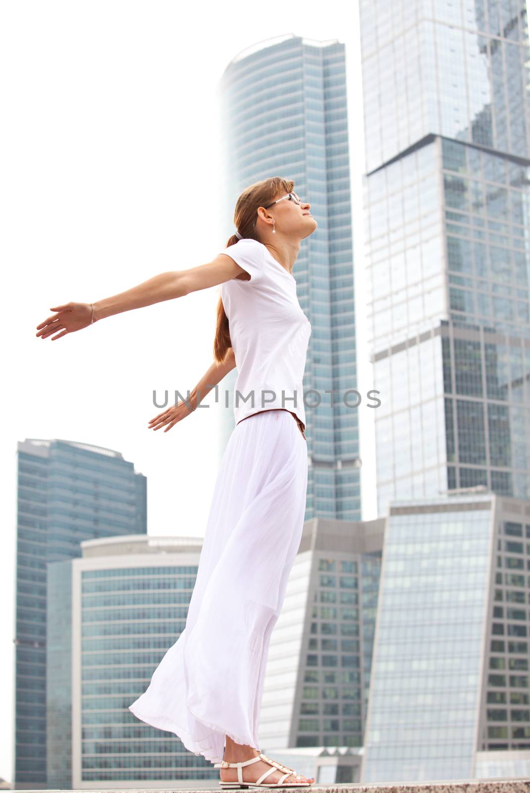 girl in white on a background of the city's skyscrapers spread her arms in the wind
