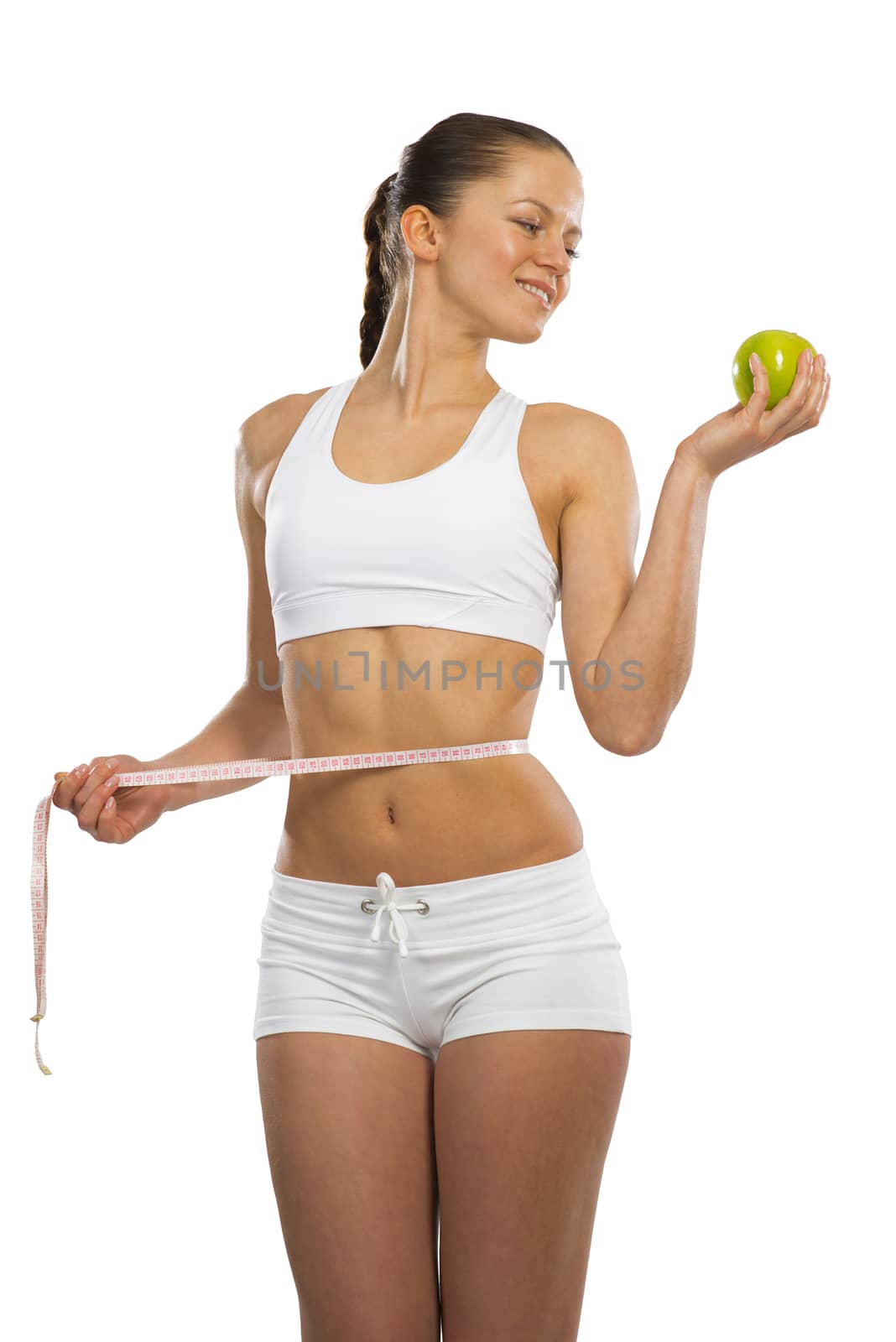 young athletic girl measuring waist measuring tape and holding a green apple, concept of healthy eating, isolated on white background