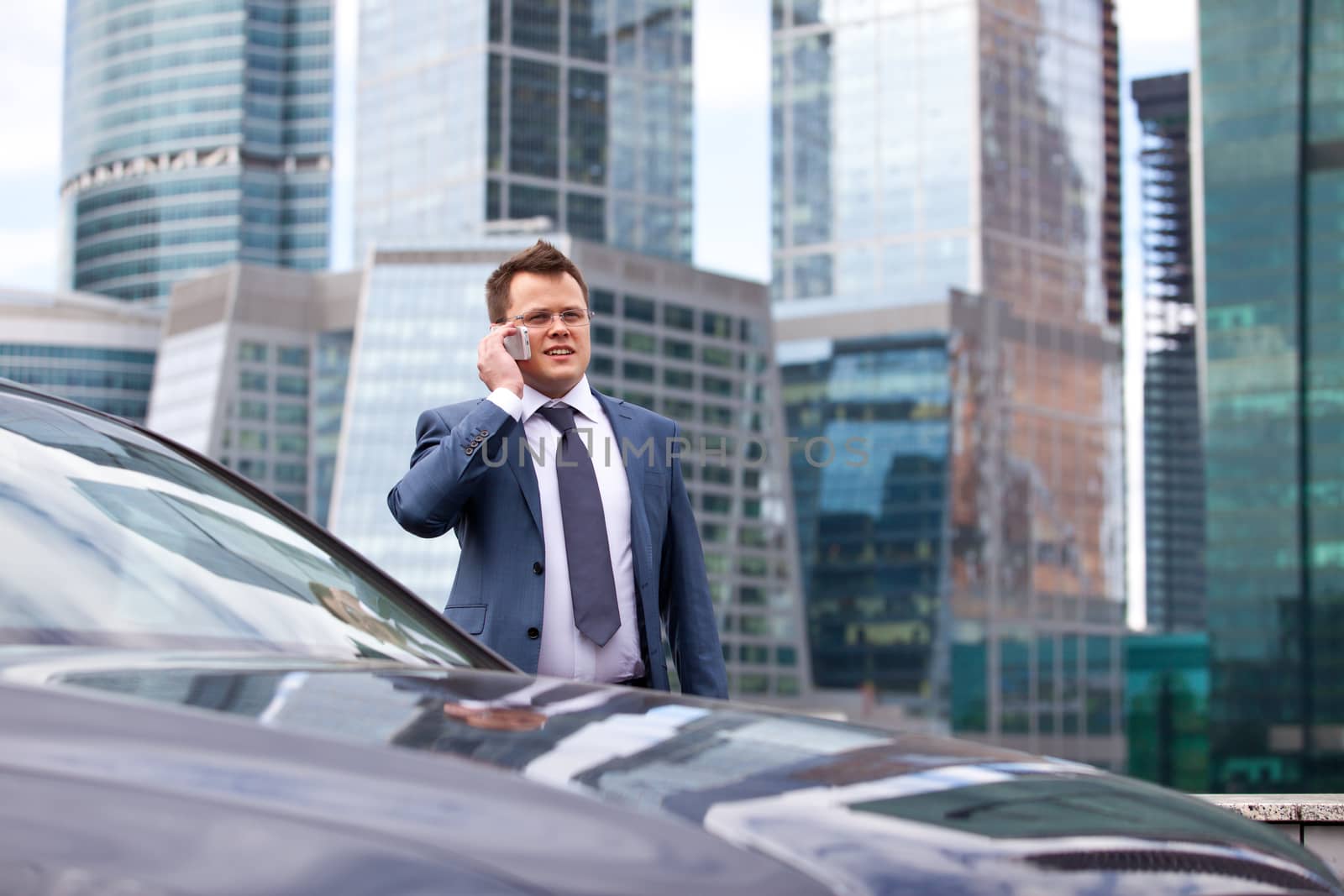successful businessman talking on the phone near the car, on the background of office buildings