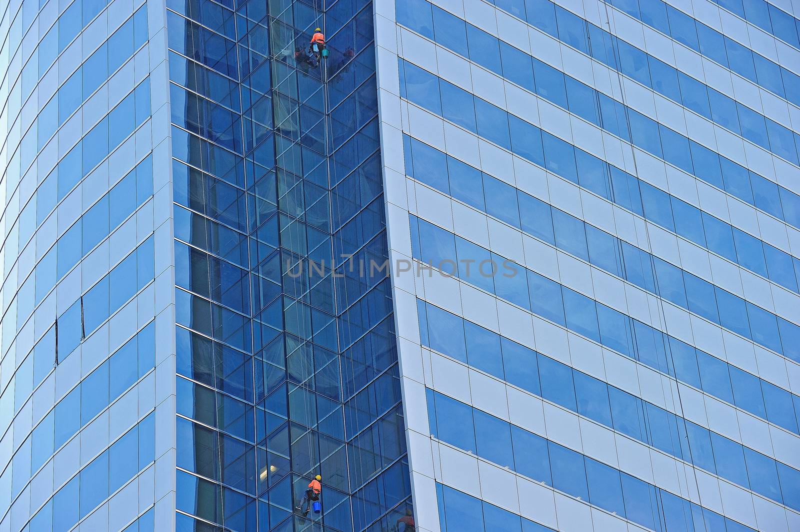Workers suspended on a scaffold high up on a blue glass skyscraper