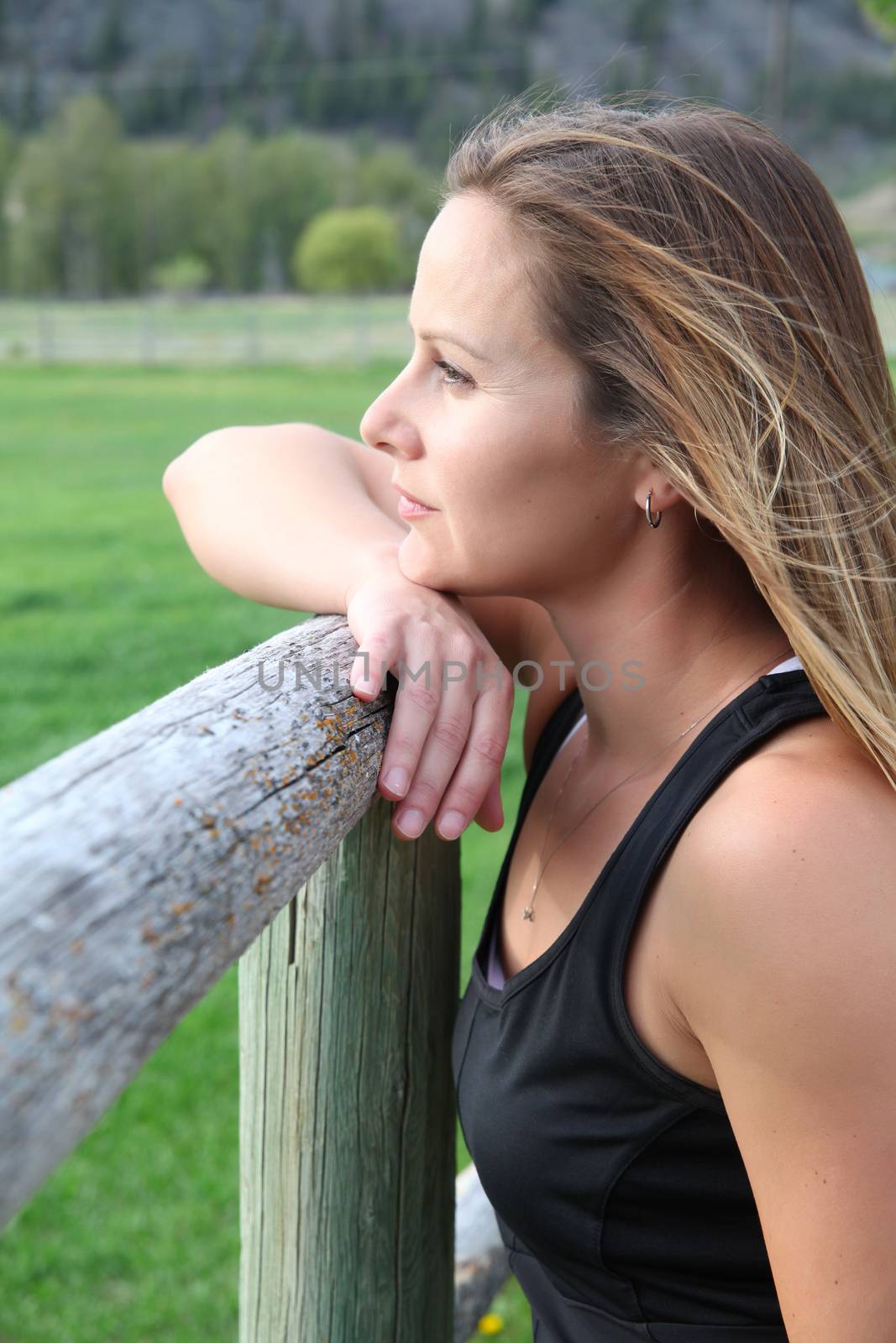 Beautiful female leaning against wooden fencing looking out
