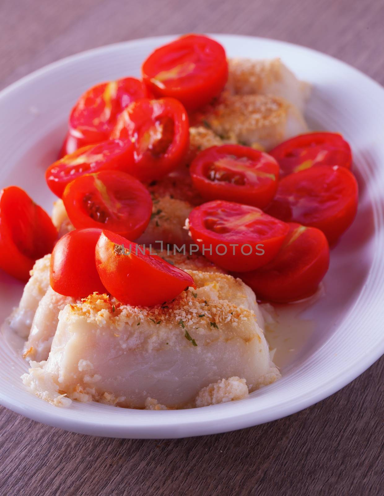 Hake au gratin with tomatoes over white plate