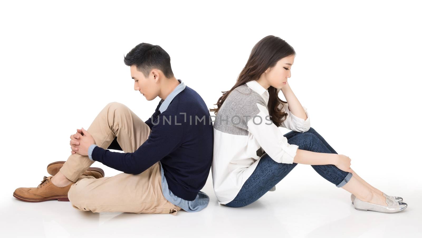 Young Asian couple sit on ground back to back with unhappy expression on studio white background.