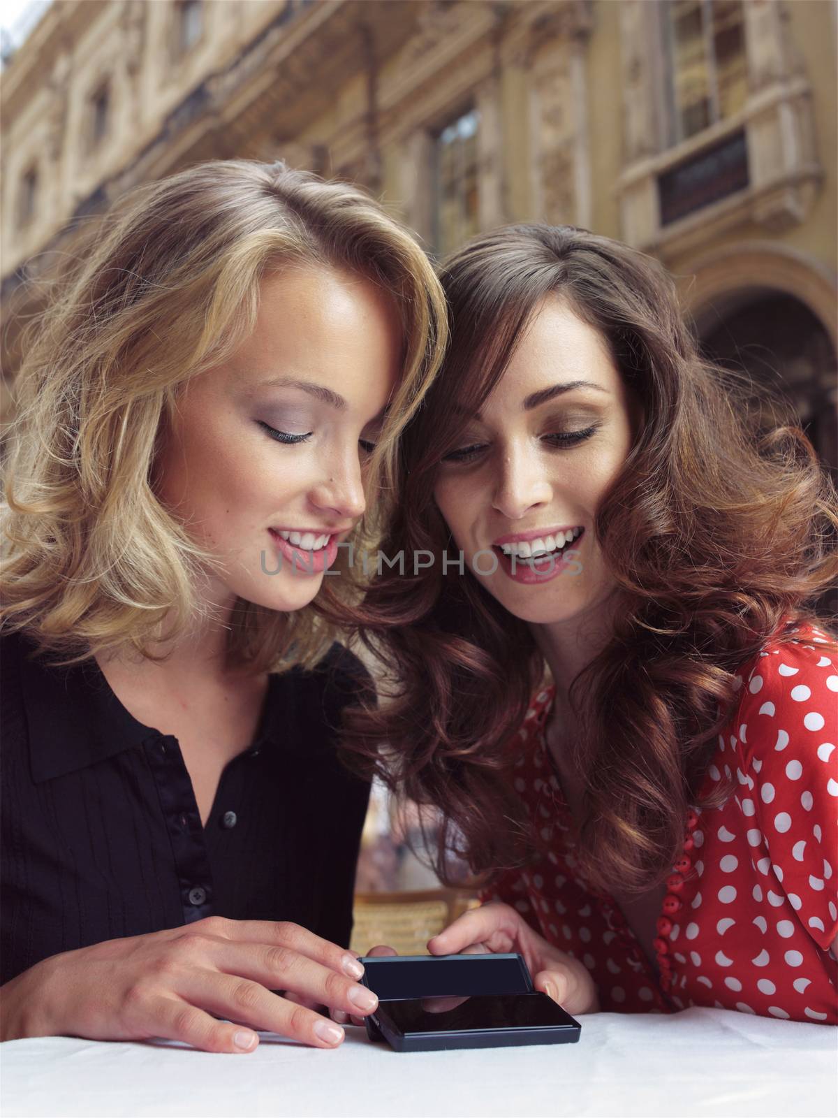 two happy girlfriends look at the mobile phones in cafe