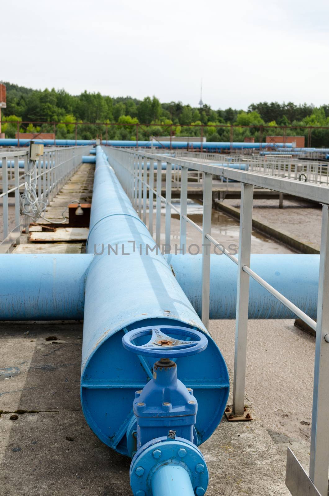 Blue stopcock tap valve gate and pipes in water treatment plant and dirty liquid bubble in background.