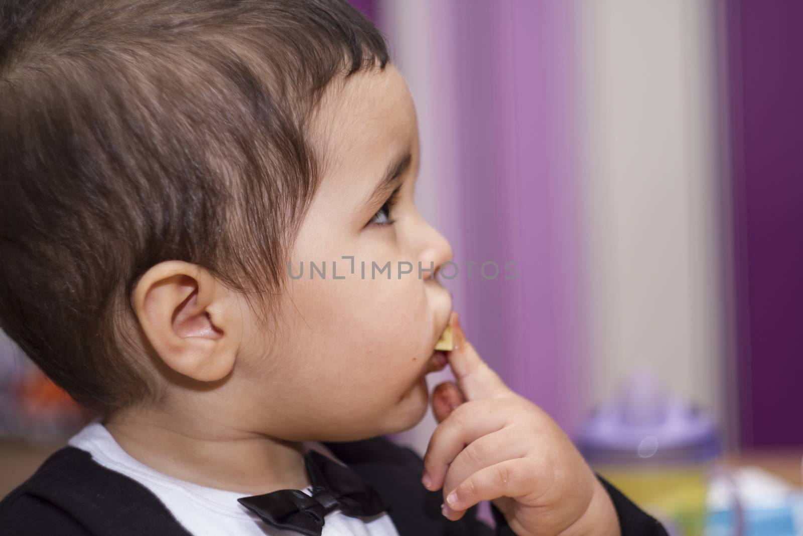 Adorable happy baby eating chocolate, wearing suit and bow tie by FernandoCortes