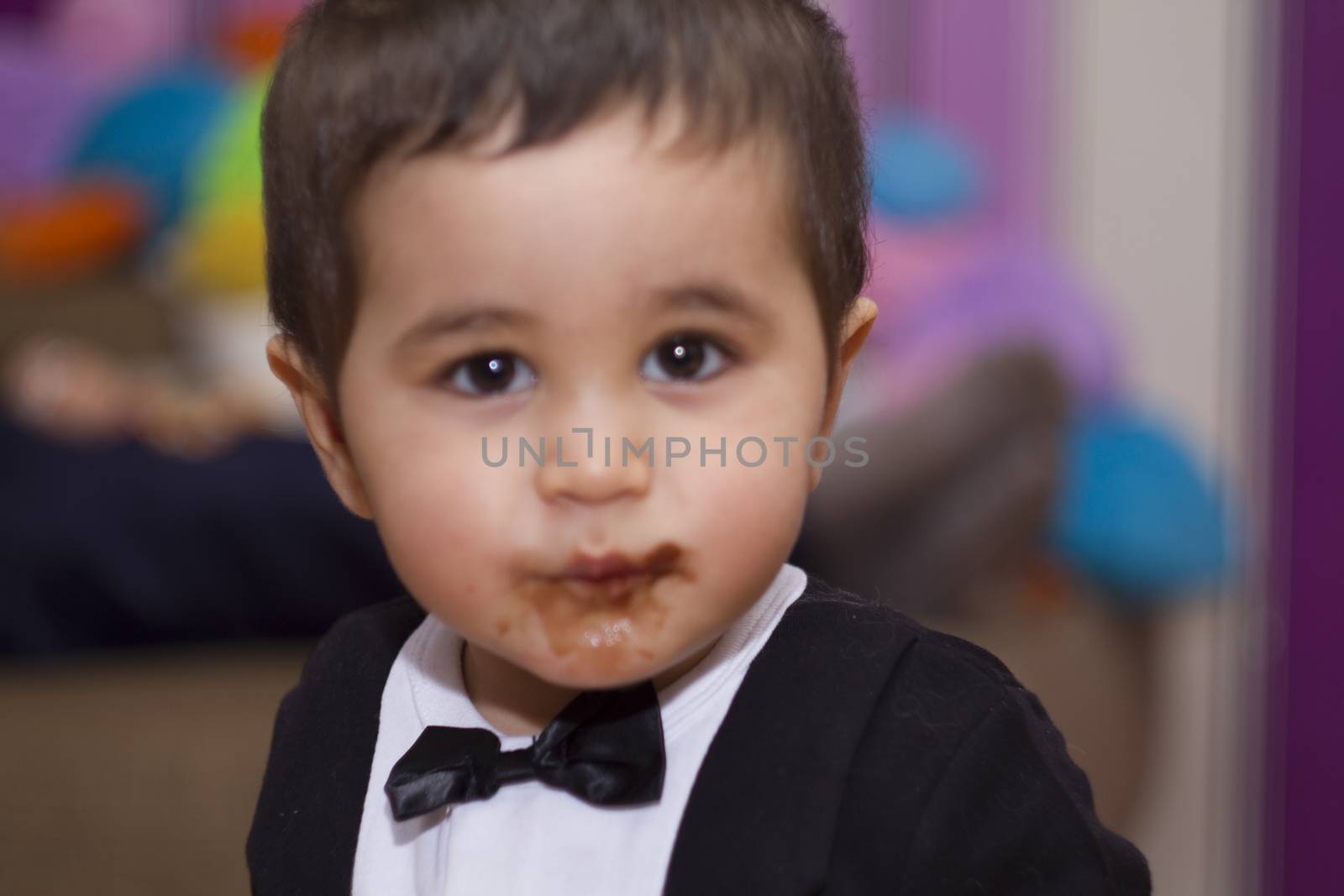 Adorable happy baby eating chocolate, wearing suit and bow tie