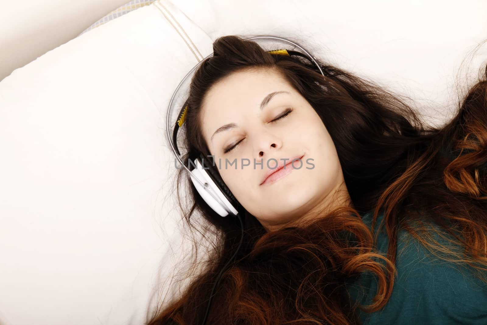 A young adult woman listening music with headphones in bed.