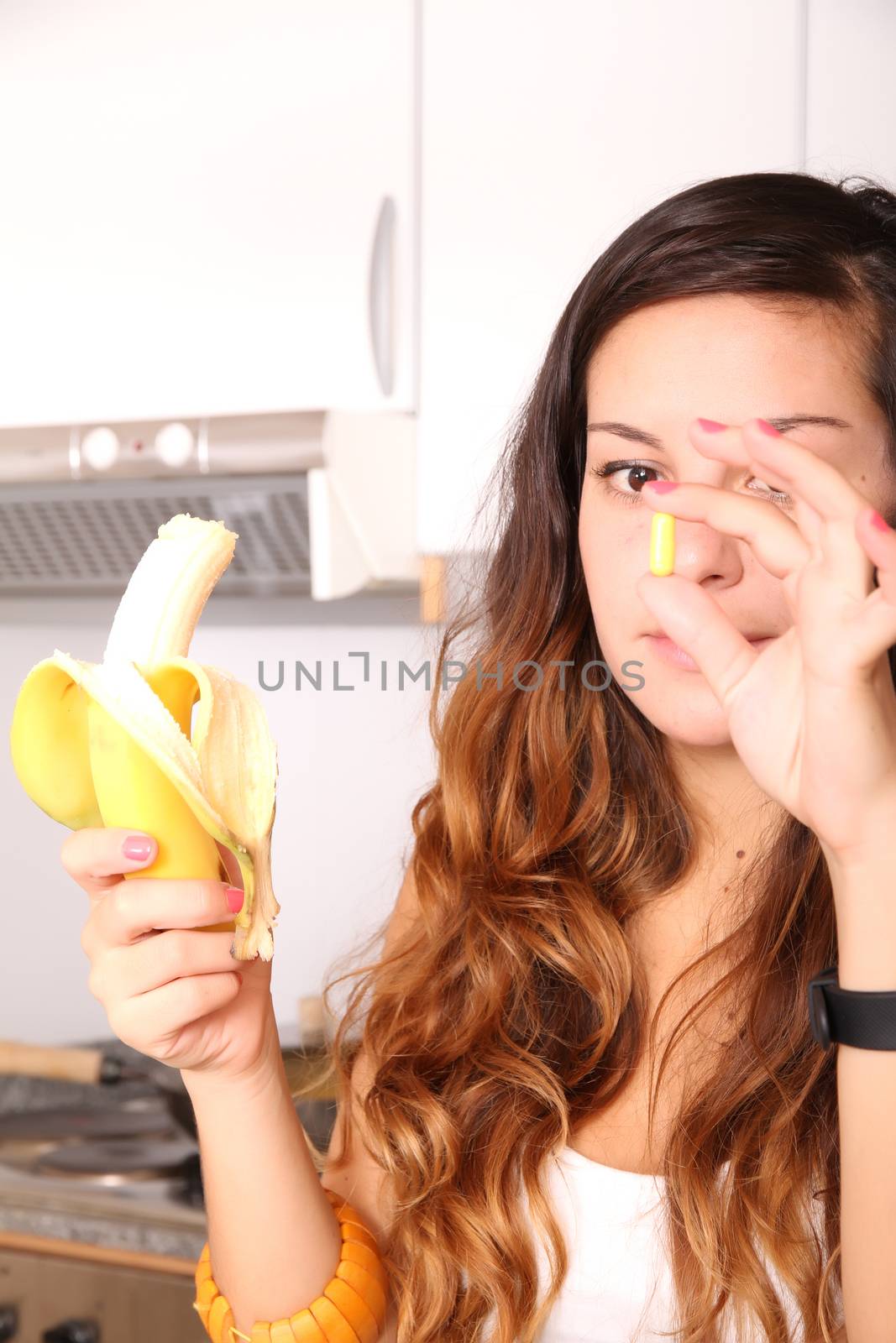 A young woman holding a supplement pill in one hand and a banana in the other.