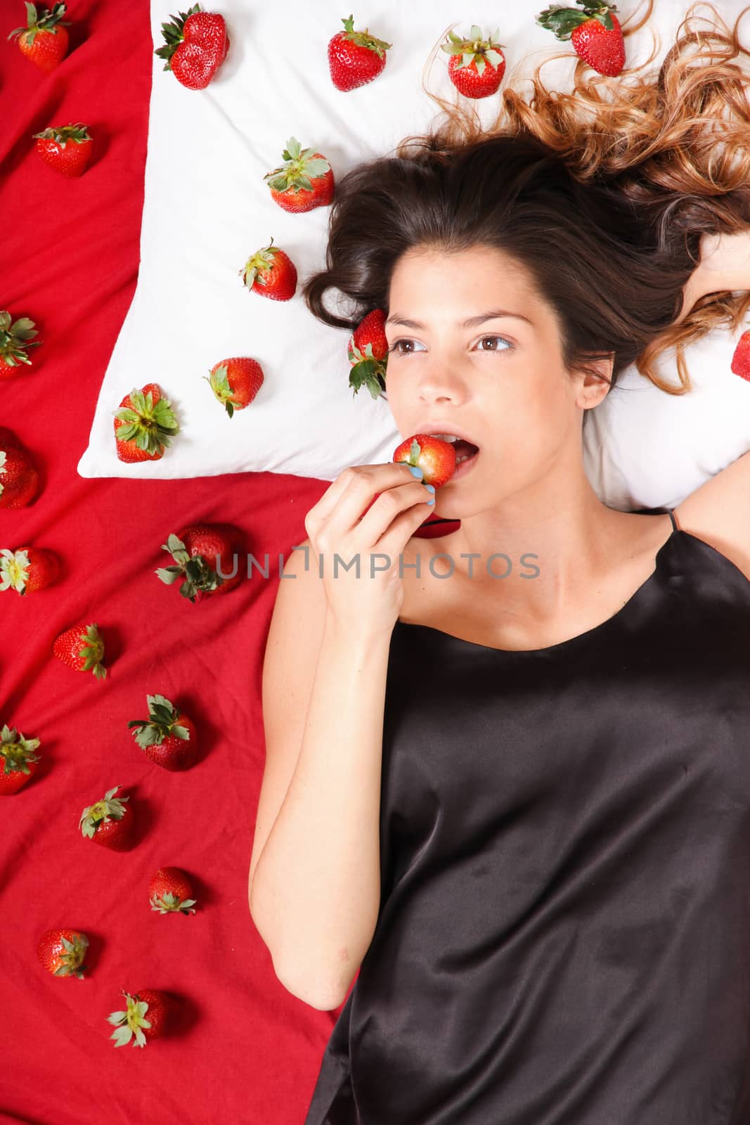 Beautiful, latin Woman eating a Strawberry in bed.
