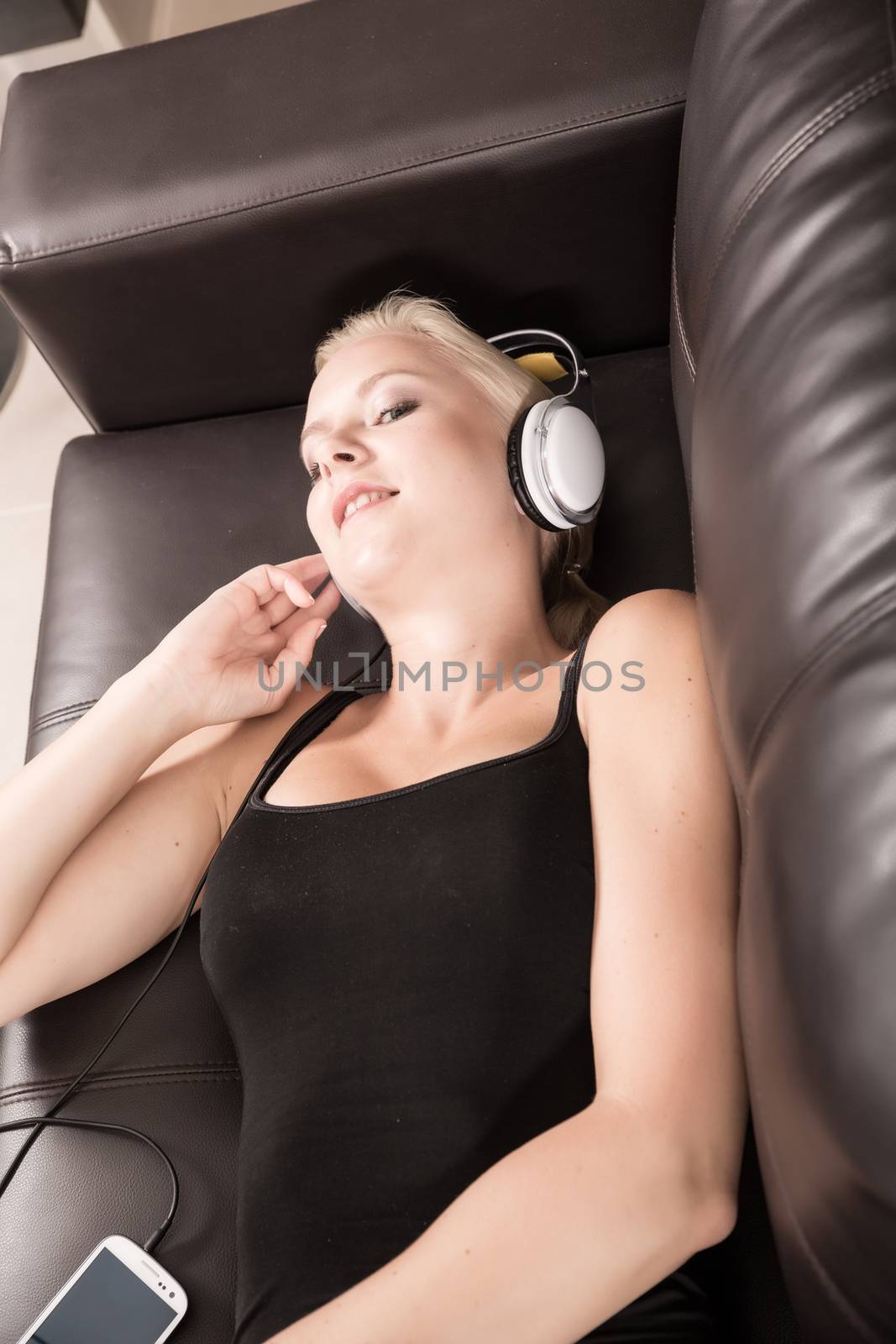 A blonde girl with Headphones laying on the sofa.