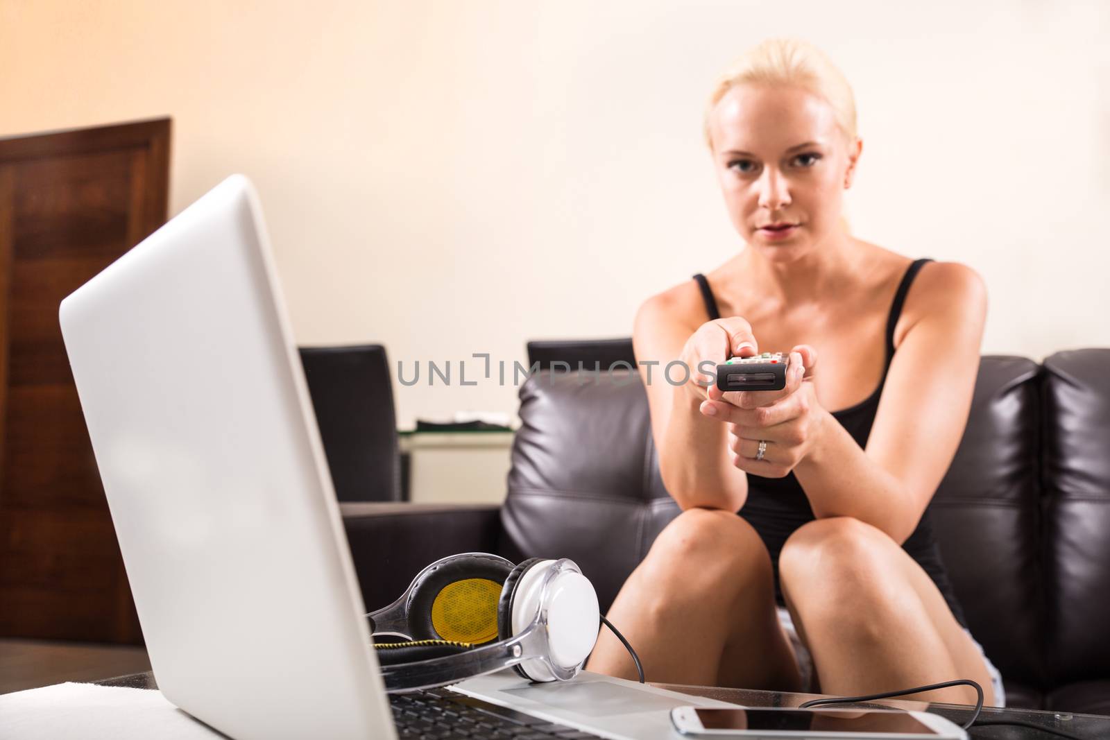 A blonde girl watching TV with the remote control in her hands
