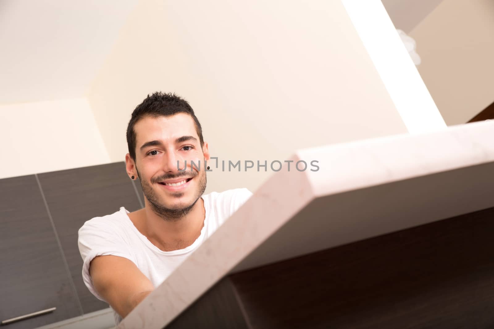 A young hispanic adult sitting thoughtful in the kitchen.