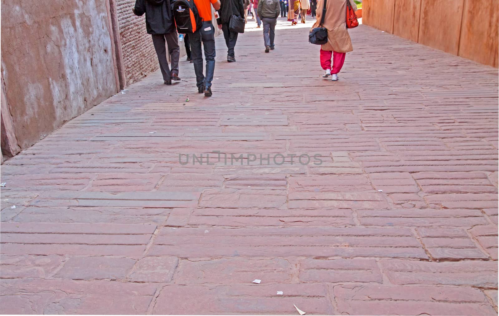 Paved tiled path enclosed by high walls with group of people walking away showing them from behind