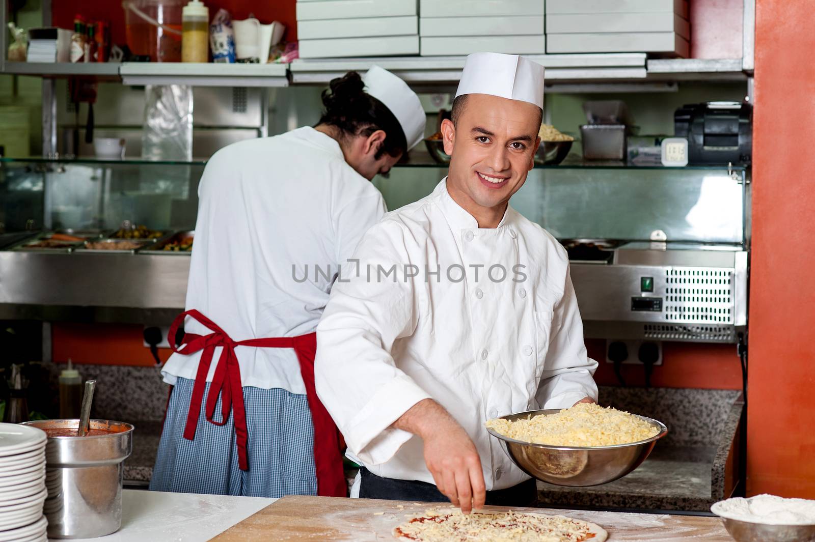 Happy chef giving finishing touch to pizza in kitchen