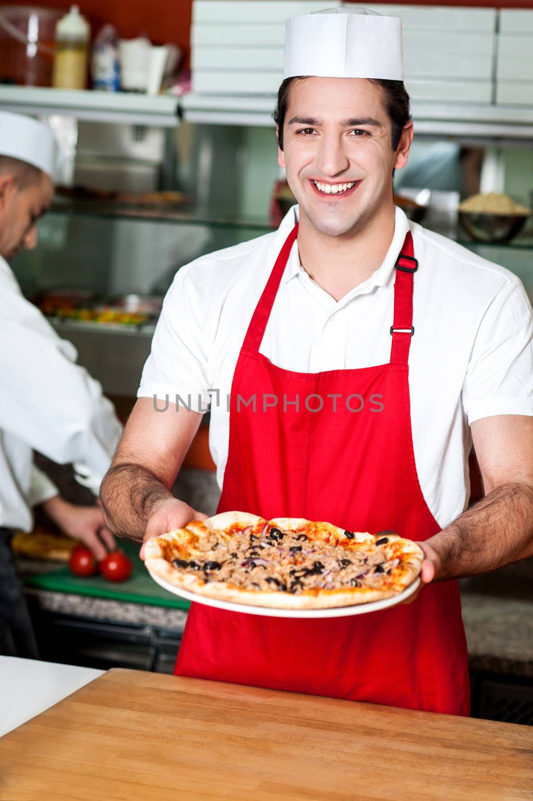 Smiling young male chef handing over pizza