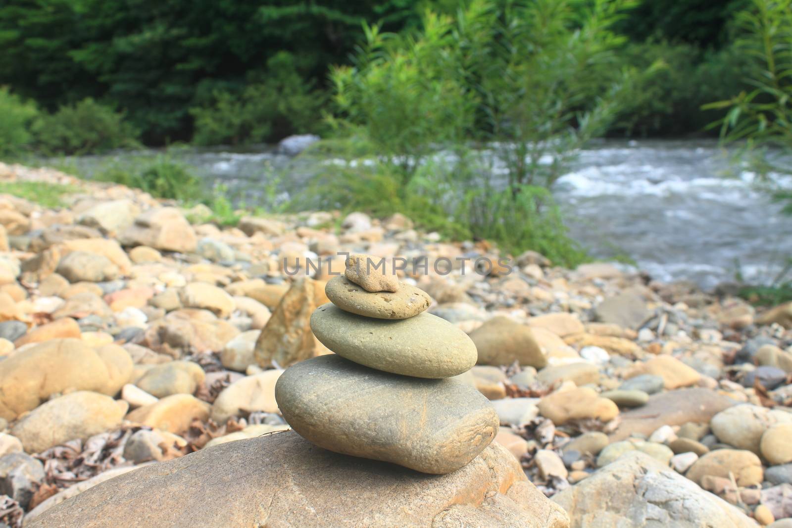 Stones pyramid near small river symbolizing zen, harmony, balance