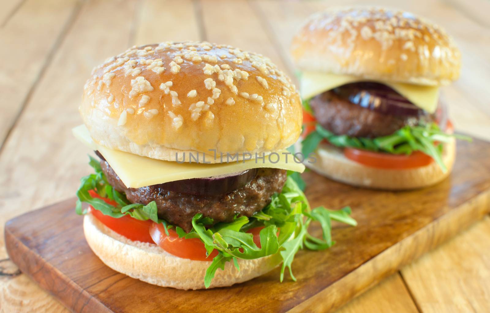 Two hamburgers with cheese and tomato filling on a cutting board