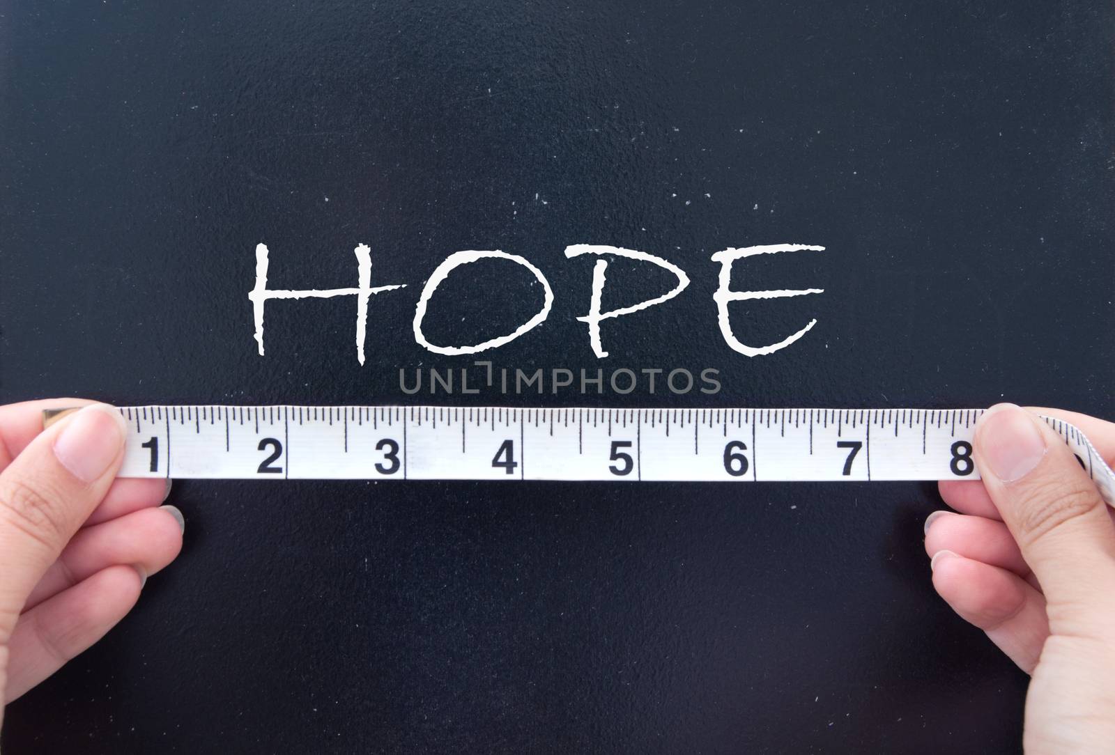 Tape measure held up against the word hope handwritten on a chalkboard