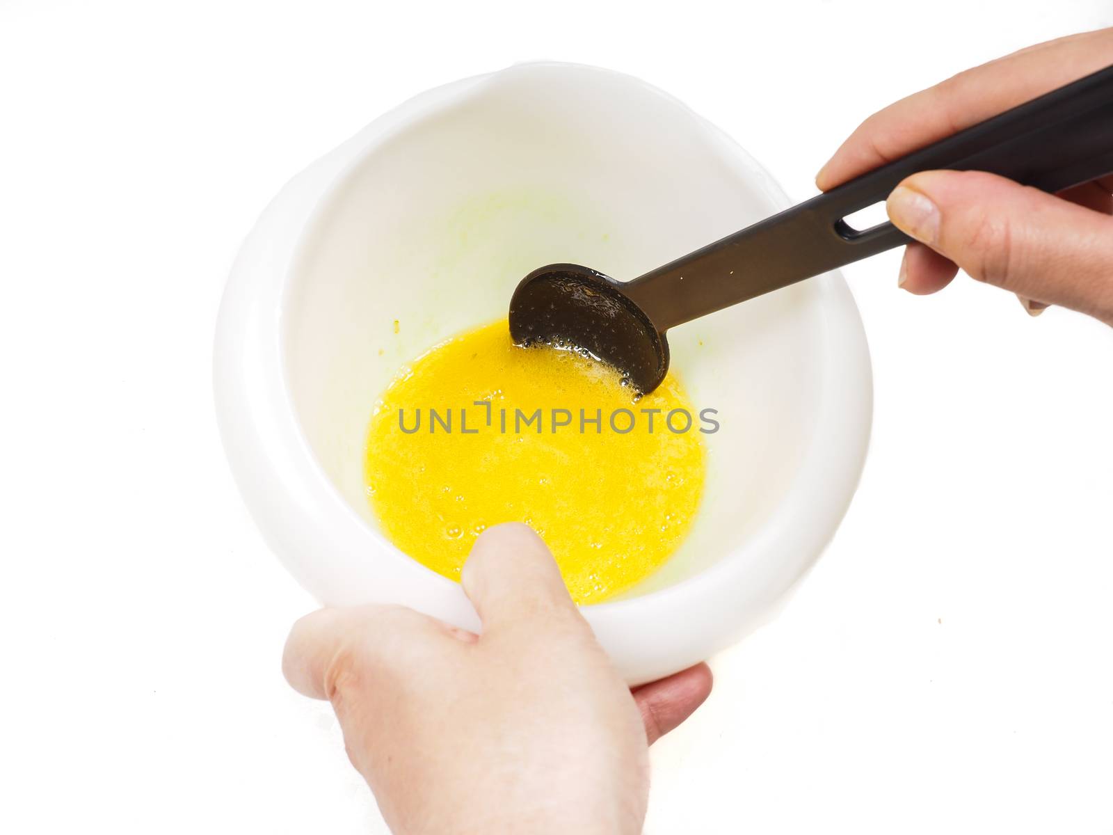 Female person mixing egg yolk and melted butter in a white bowl with a black spatula