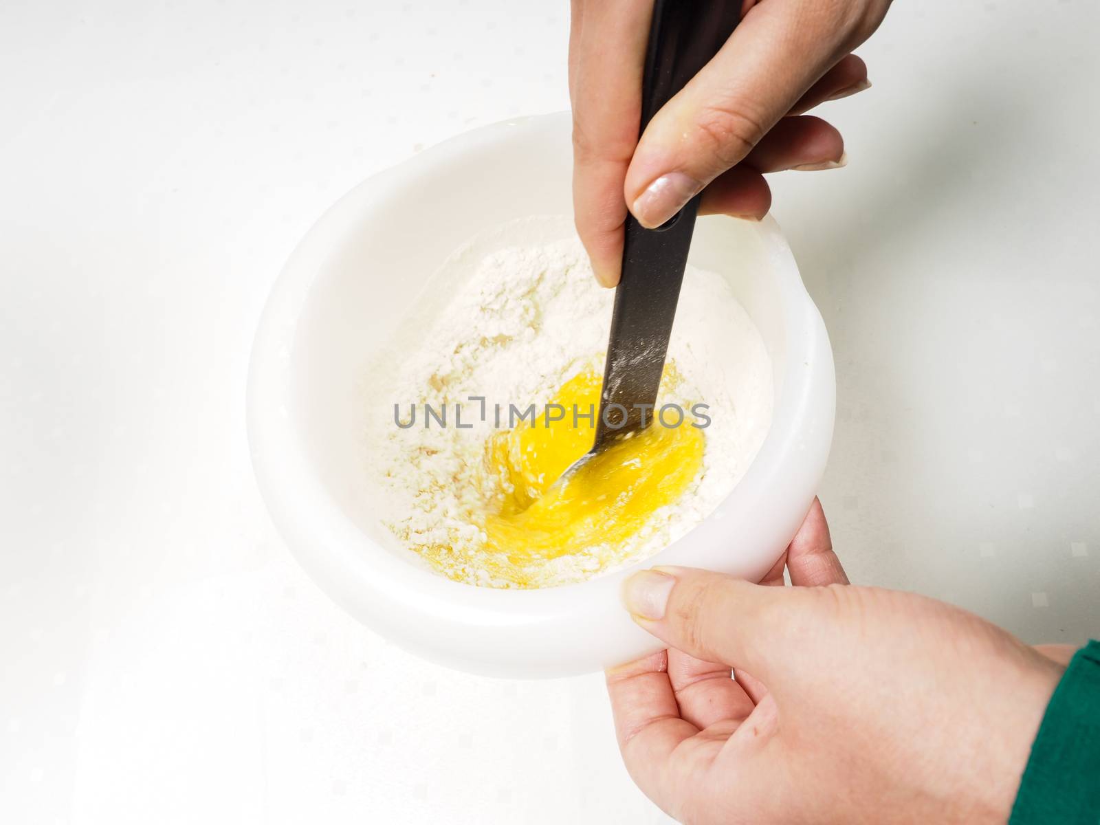 Female person blending flour with egg yolk and melted butter with a black spatula in plastic bowl