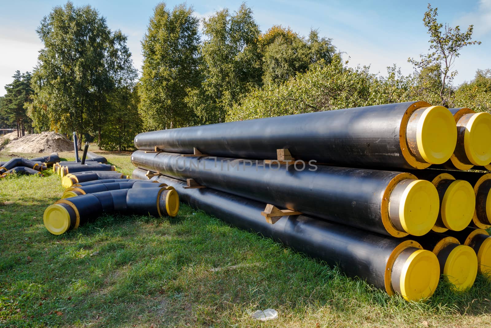 A bunch of black and yellow construction pipes layed on the ground