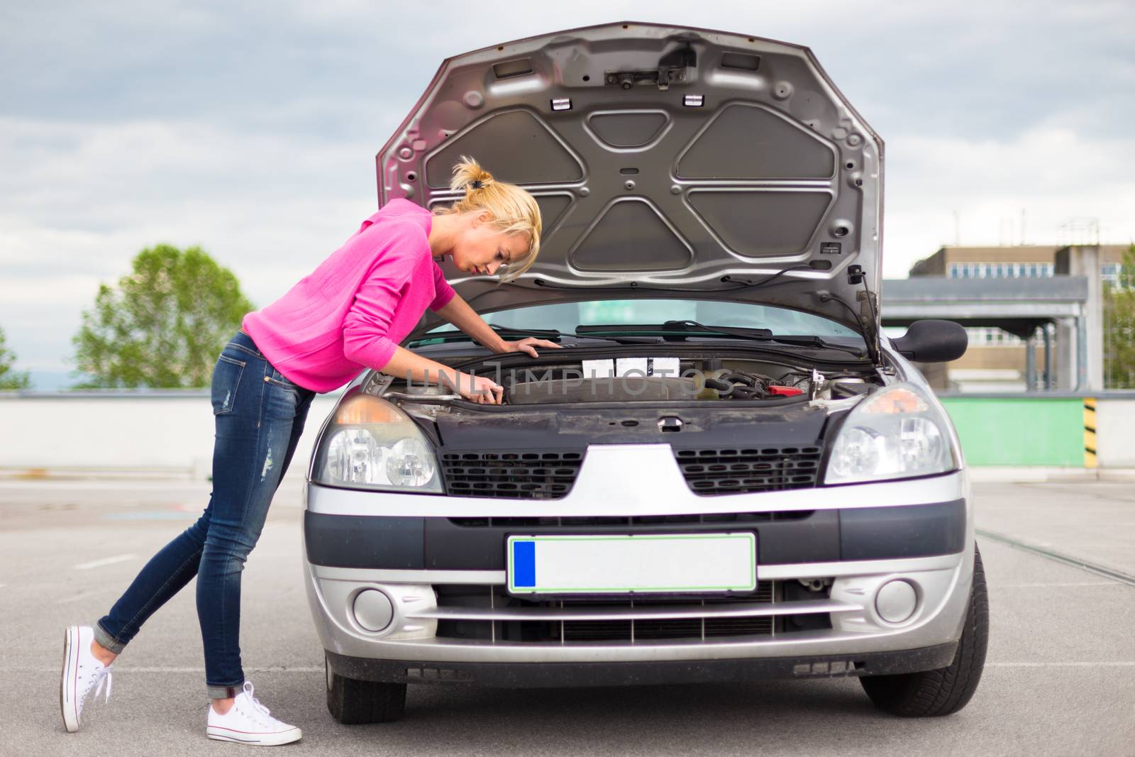 Self-sufficient confident modern young woman inspecting broken car engine.