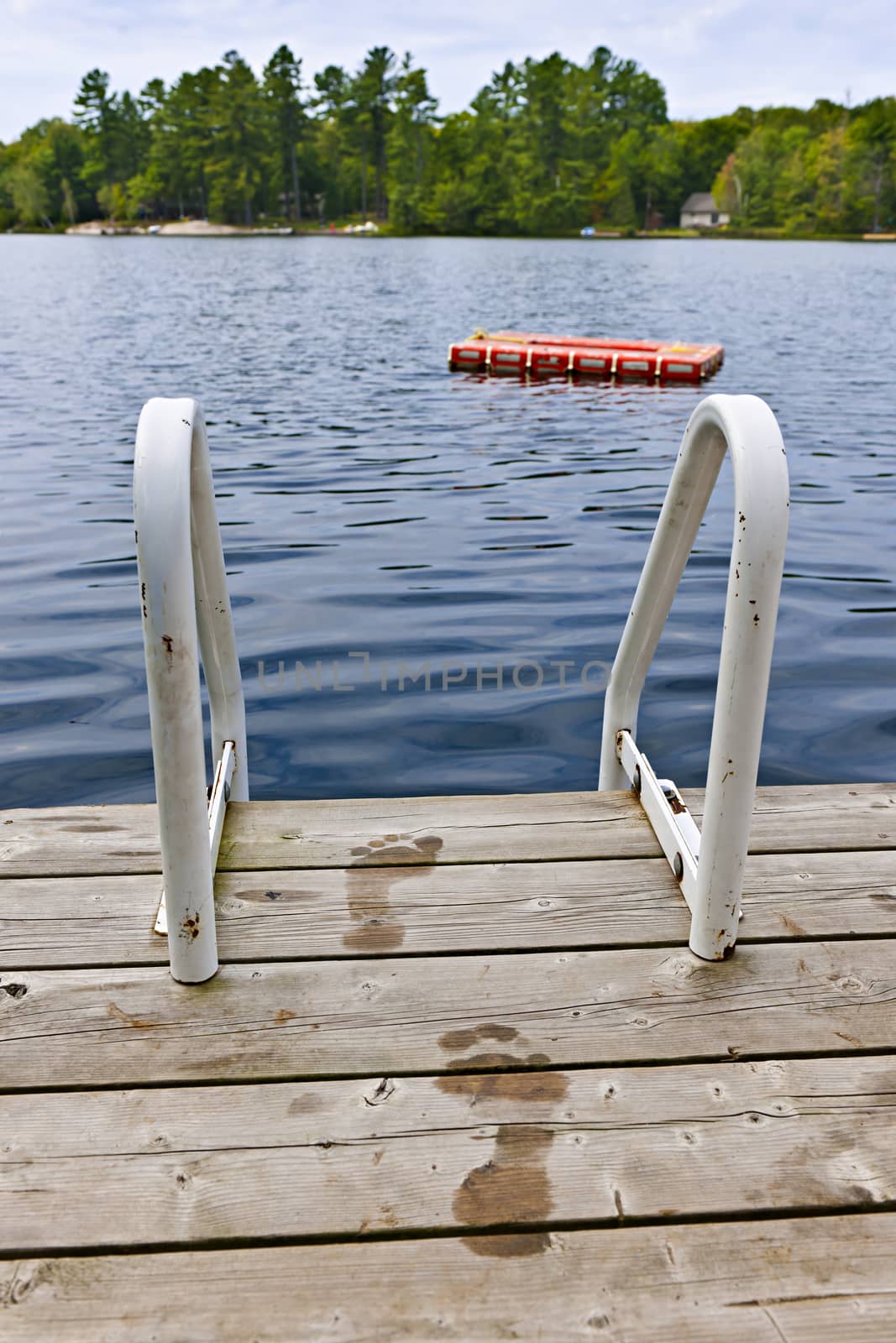 Wet footprints on dock with ladder and diving platform at lake in Ontario Canada