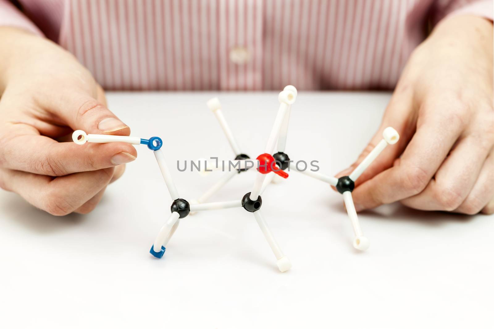 Hand of female student assembling amino acid molecule models for science project