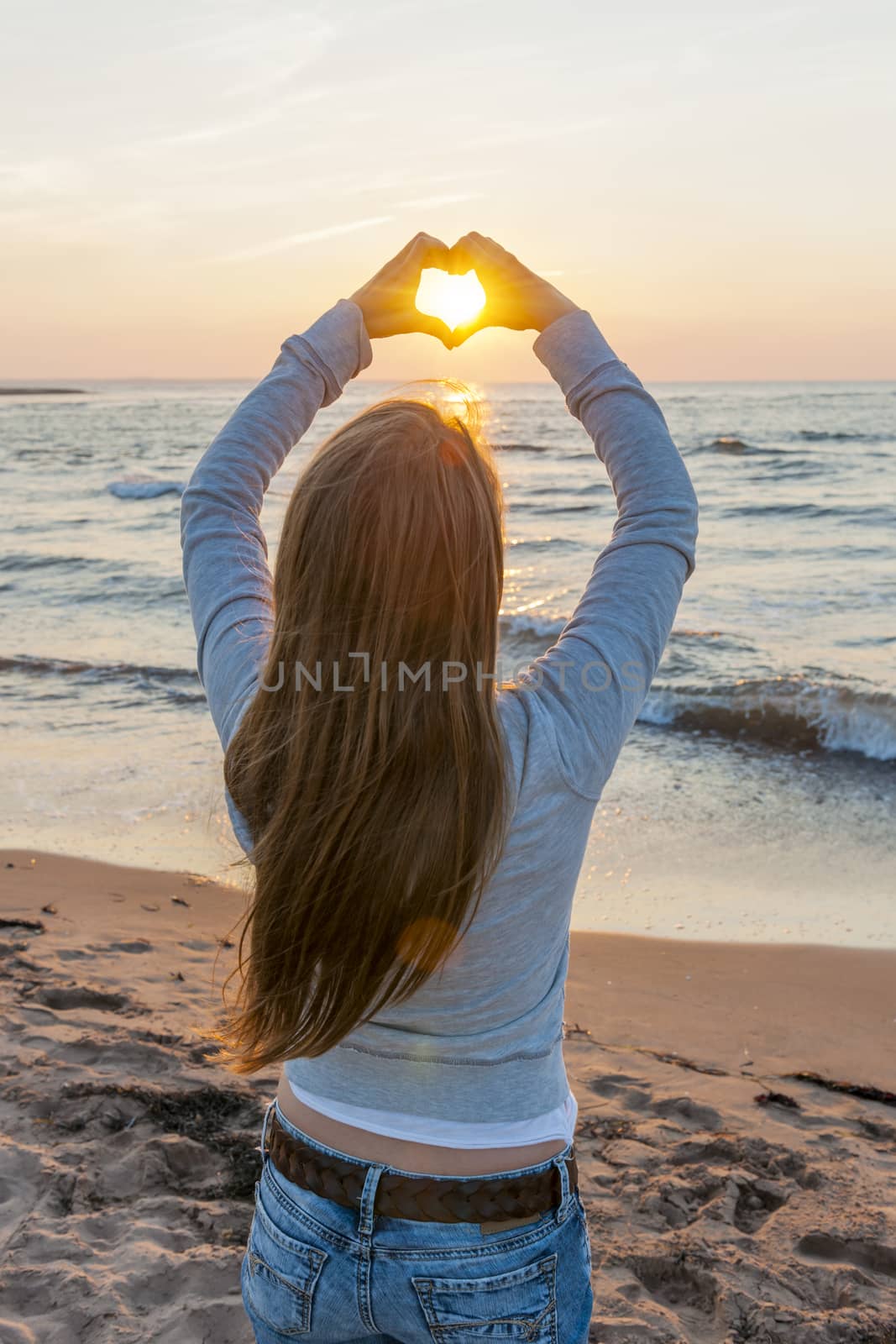 Girl holding hands in heart shape at beach by elenathewise