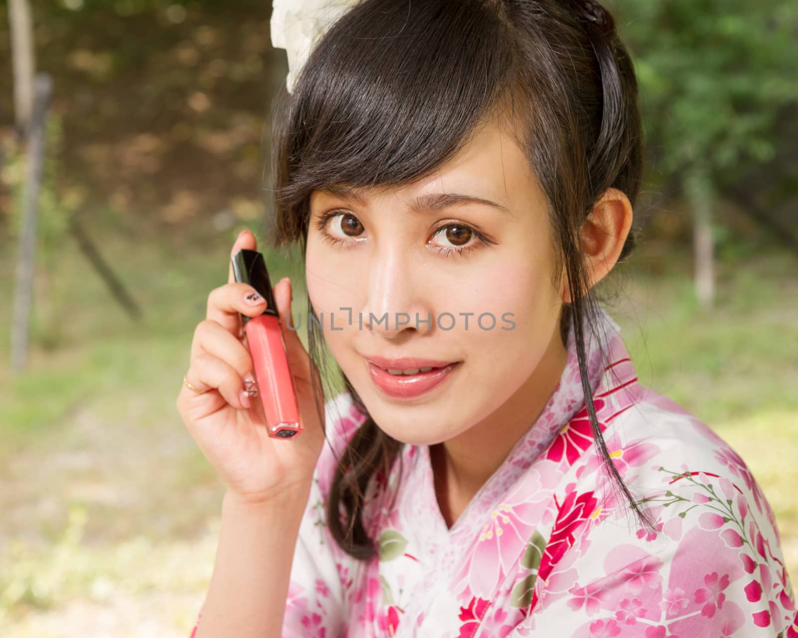 Asian woman in a kimono in a Japanese style garden holding up lip gloss