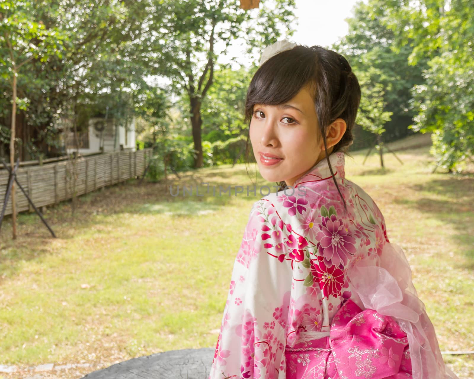 Asian woman in a kimono in a Japanese style garden looking back at camera