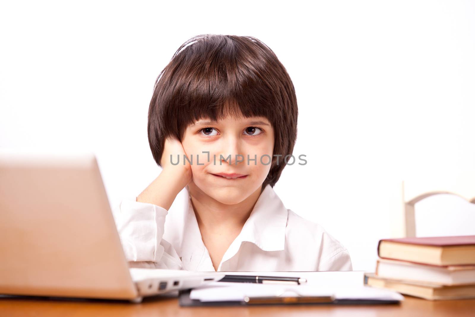 Sly boy at table with computer and books