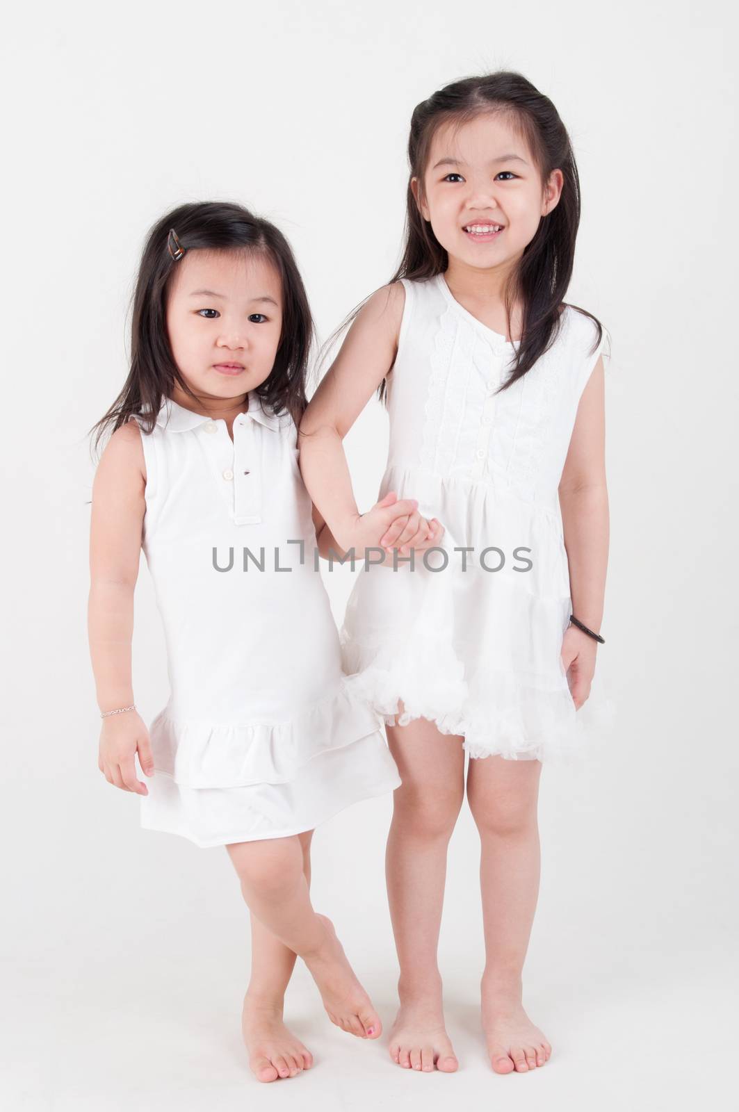 Little girls portrait. Asian sisters holding hand on plain background. Sibling love.