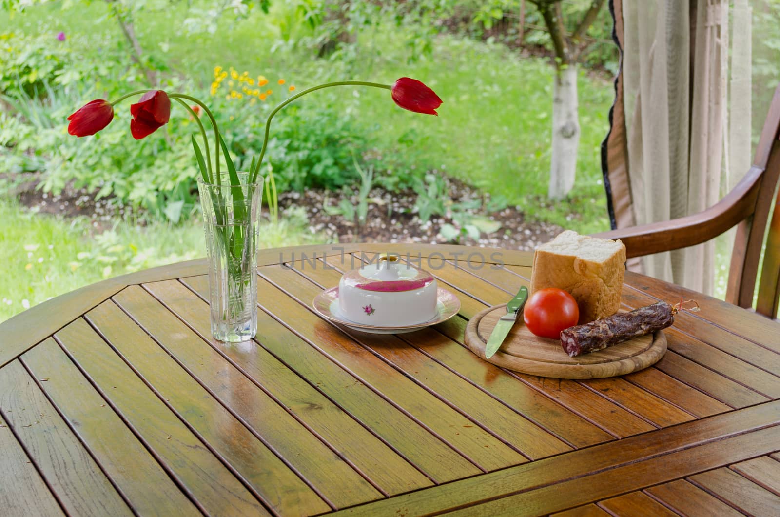 smoked sausage white bread butter for breakfast prepare and tulip flowers in vase in garden bower.