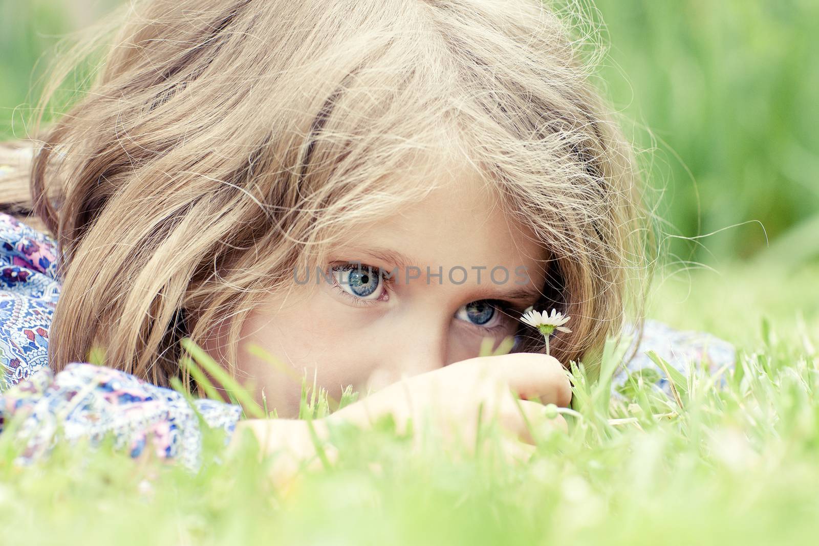 Little adorable girl lying on grass looking at daisy