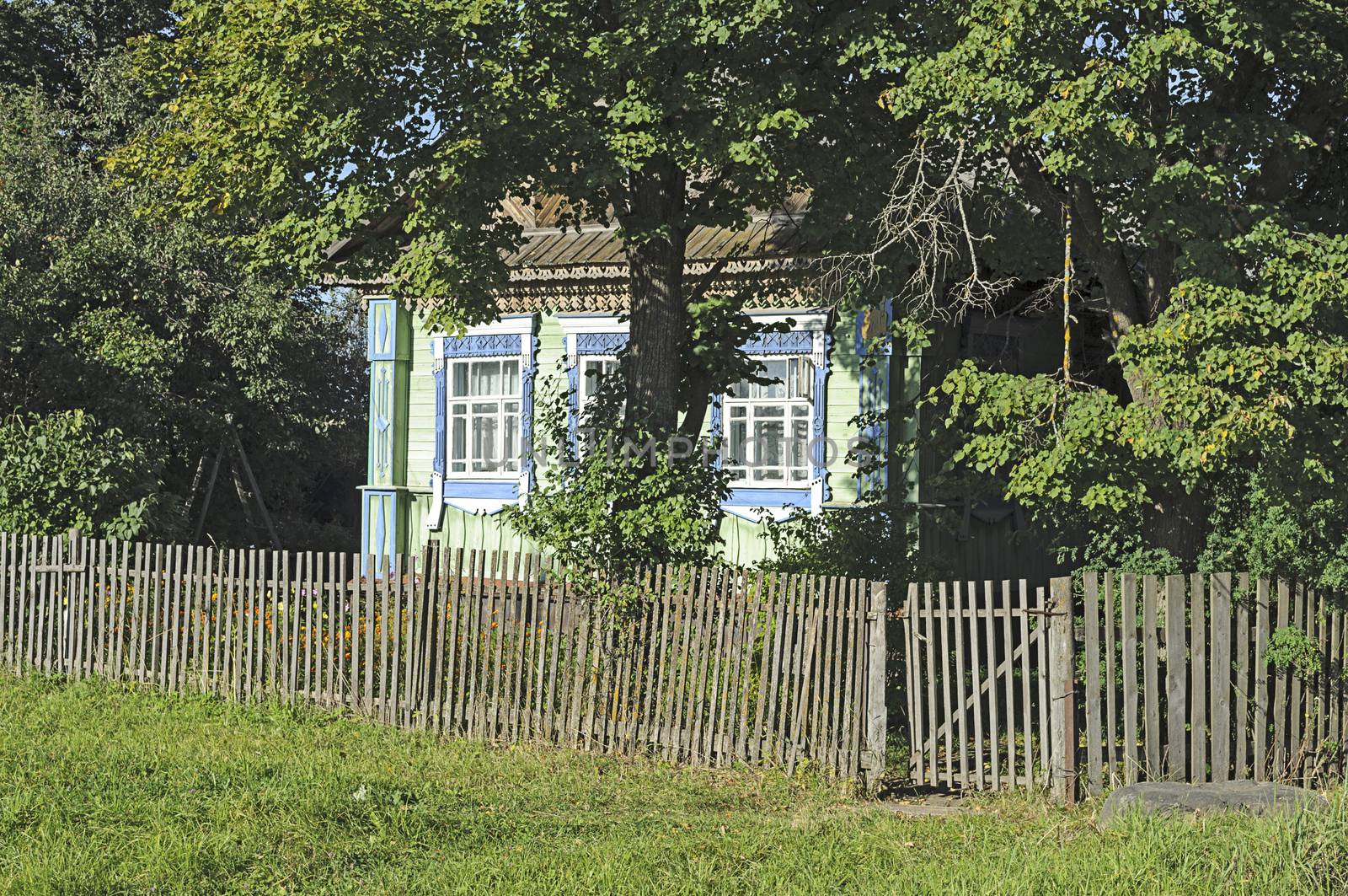 Small village house in shade of trees behind the old wooden fence