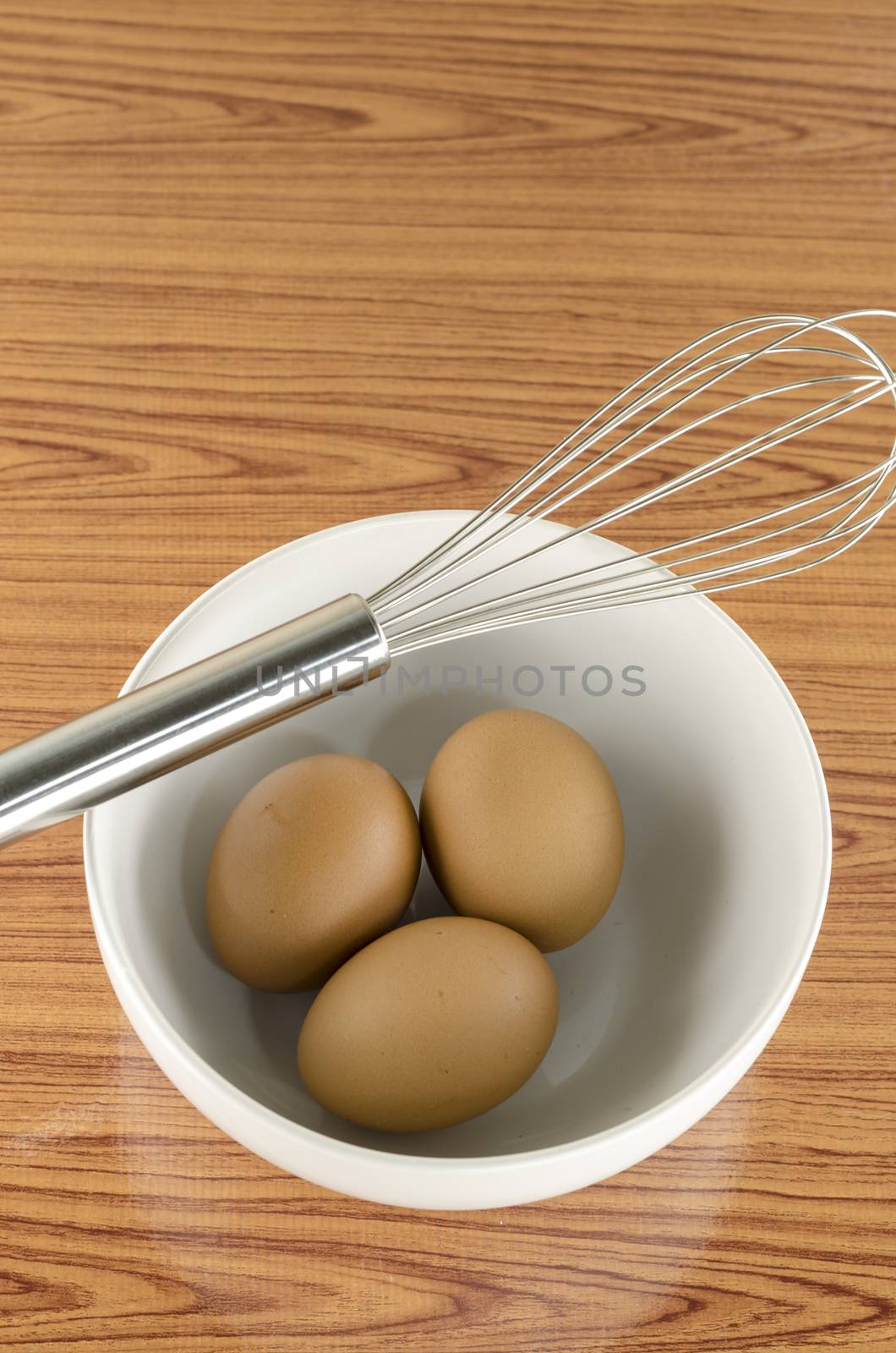 whisk and egg in white bowl on wood table background