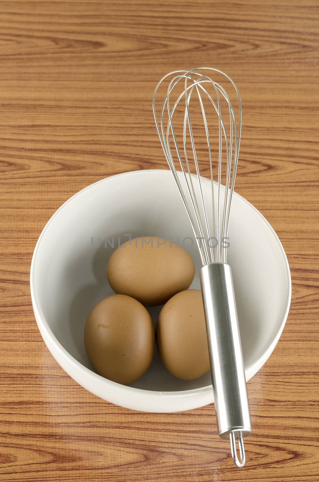 whisk and egg in white bowl on wood table background