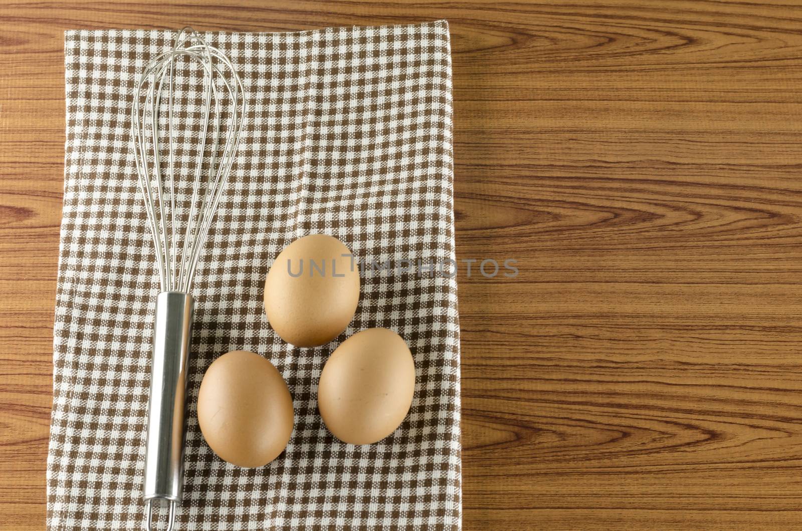 whisk egg and brown kitchen towel on wood table background