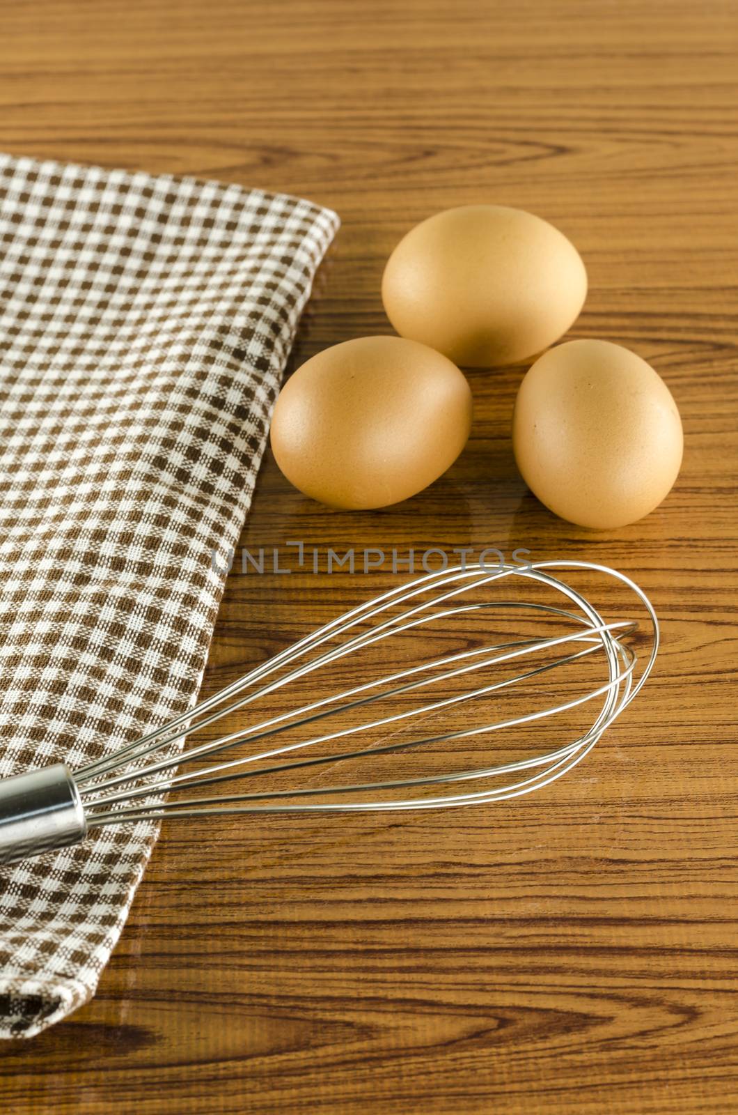 whisk egg and brown kitchen towel on wood table background