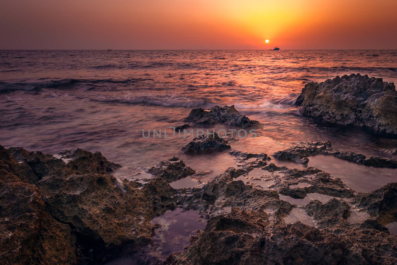 red sunset over the sea with rocks in foreground