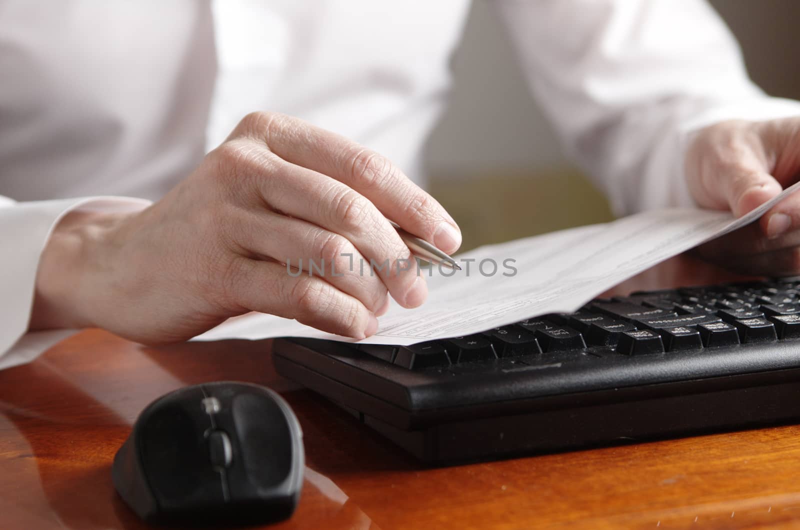 Hands with a document and a pen on a computer keyboard