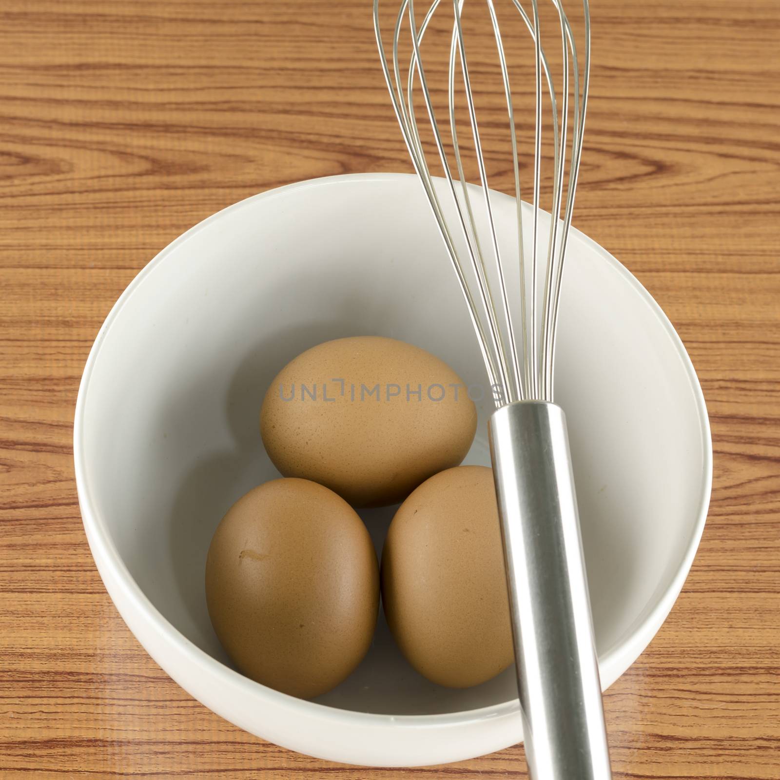 whisk and egg in white bowl on wood table background