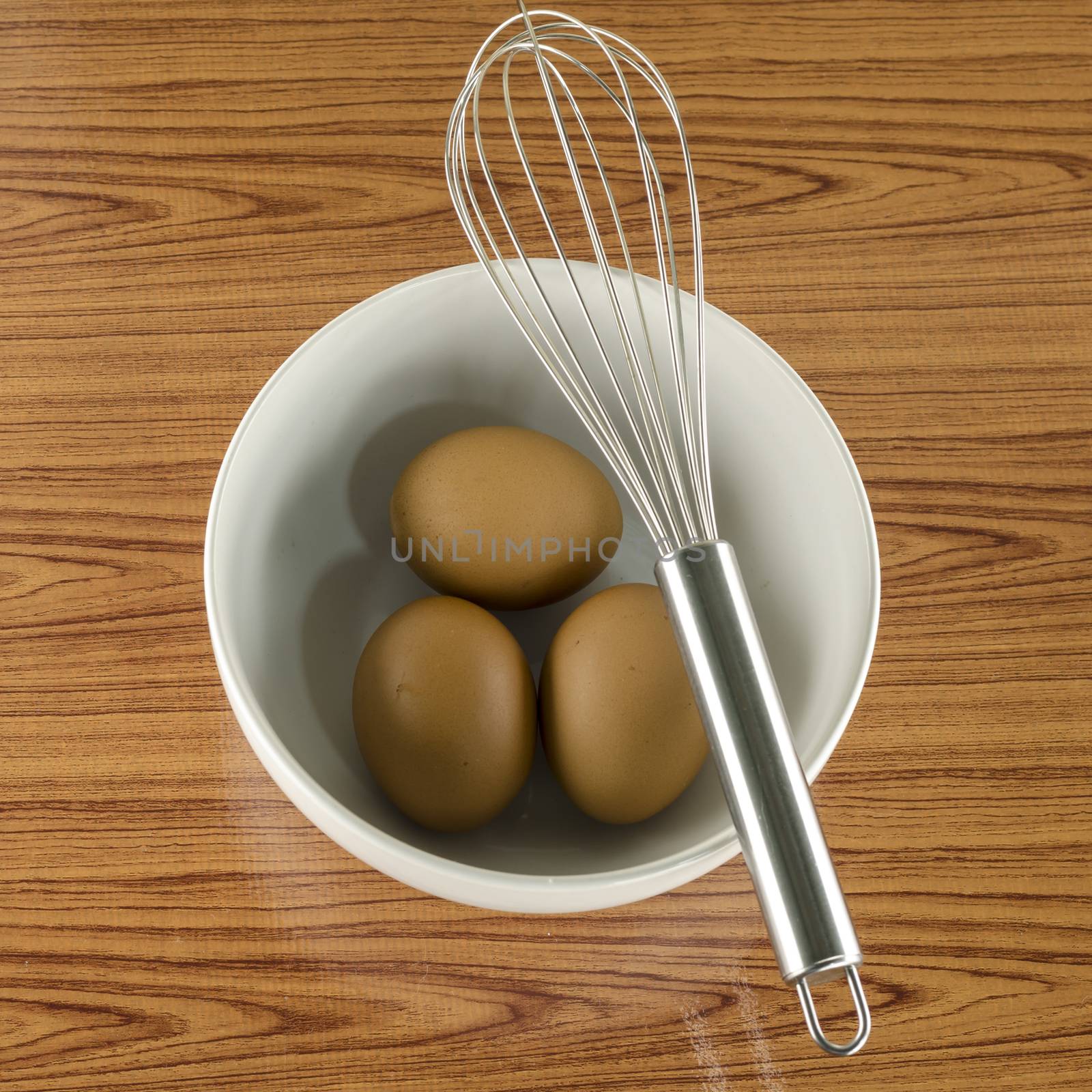 whisk and egg in white bowl on wood table background