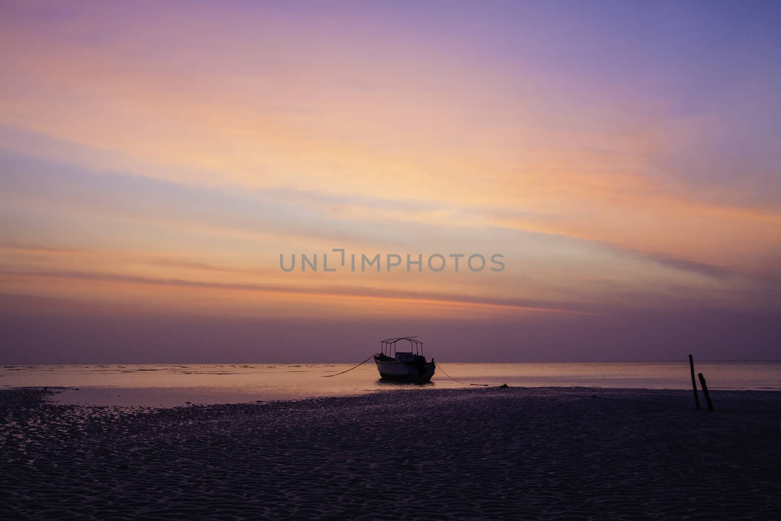 The low tide of predawn and dead calm sea has immobilised this lone motor boat anchored near shoreline while the approaching dawn is reflected by the various hues of blue and orange in the sky. the sandy beach in foreground and the two stakes on right stabilize the composition.
