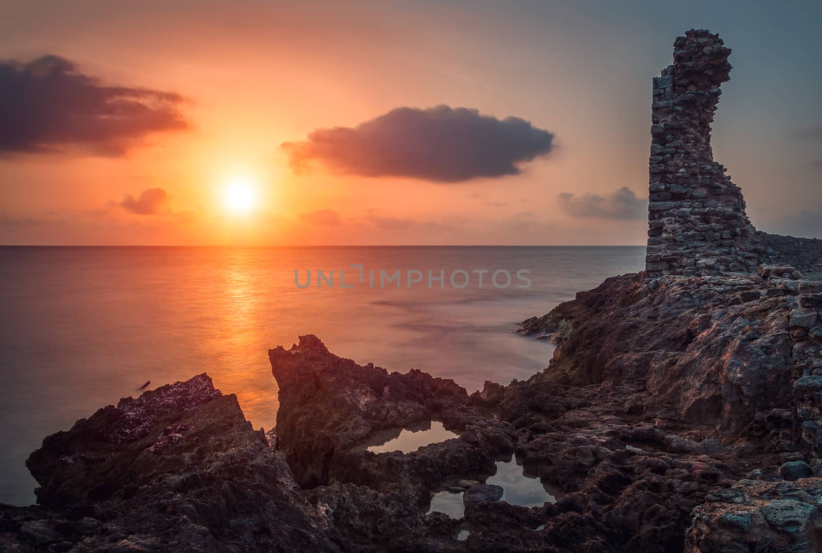 sunset over the sea and rocky coast with ancient ruins