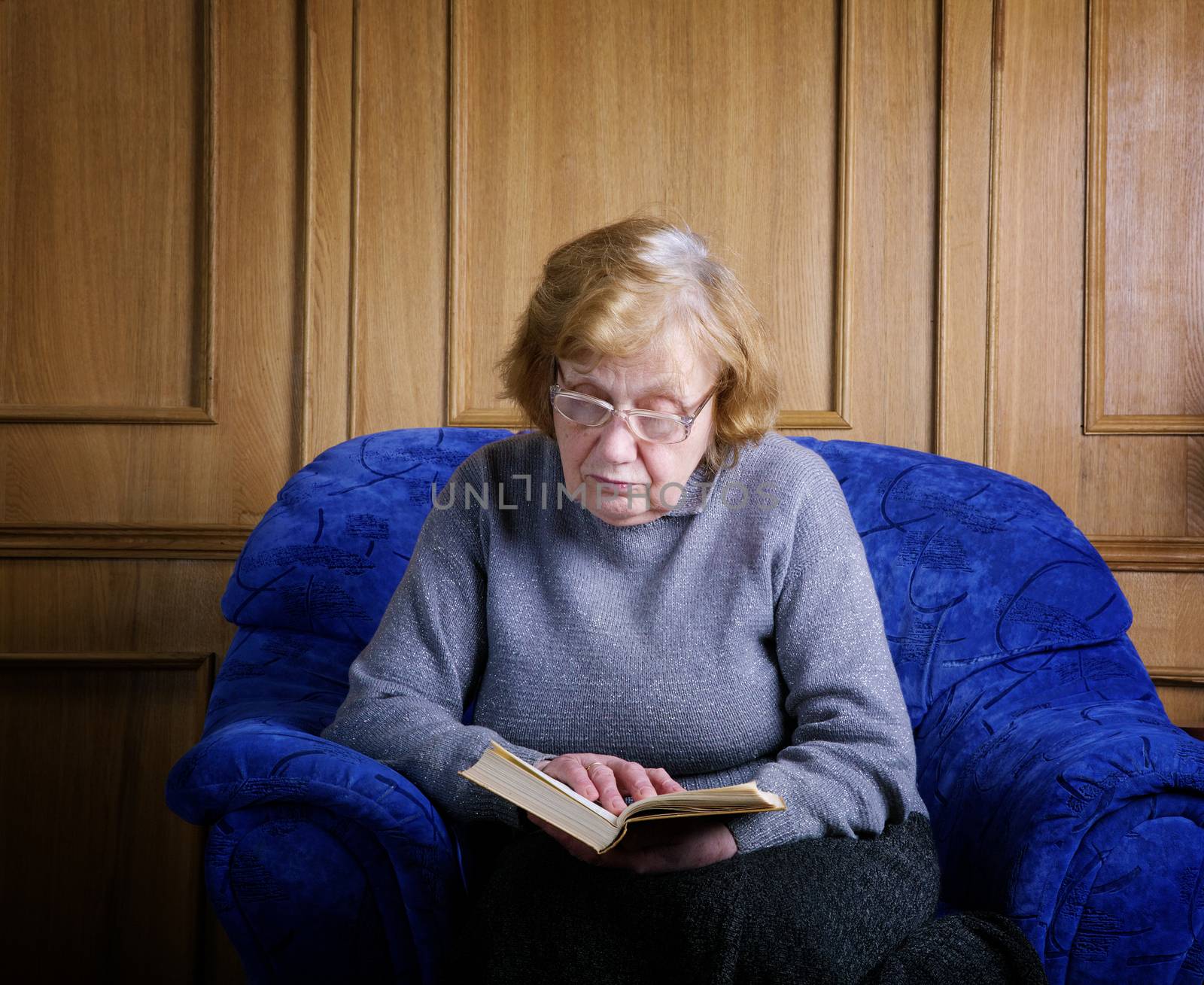 The old woman sits in an armchair and reads the book